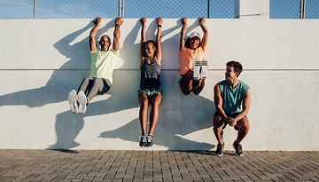 Vier Personen, die an einer Wand trainieren, lächeln und sind in Fitnessaktivitäten engagiert.